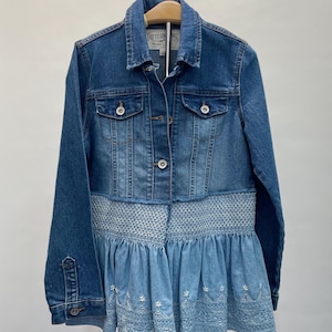 May include: A blue denim jacket with a white embroidered ruffle hem. The jacket has a button closure and two front pockets. The label on the jacket reads "Tattertots".