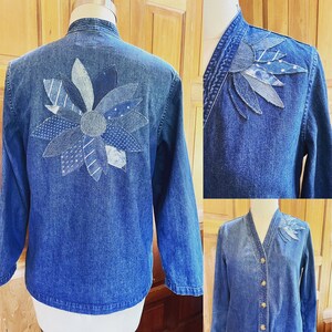 May include: A denim jacket with a large flower design made from different shades of blue denim patches. The jacket has a collar and long sleeves.