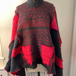 May include: A gray and red knitted poncho with a zipper closure and decorative red patches. The poncho has a high neck and a loose fit.