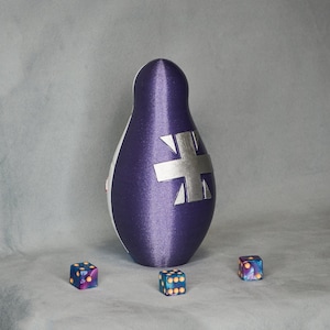 May include: A purple and white fabric nesting doll with a silver Union Jack design. Three small dice with blue, purple, and yellow spots are in front of the doll.
