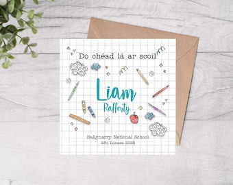 May include: A white card with a blue grid pattern and colorful drawings of school supplies. The text "Do chéad lá ar scoil" is at the top of the card. The name "Liam Rafferty" is written in blue text. The text "Ballynarry National School" and "28ú Lúnasa 2025" is at the bottom of the card.
