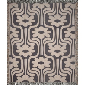 May include: A woven throw blanket with a geometric pattern of stylized flowers in beige on a dark gray background.