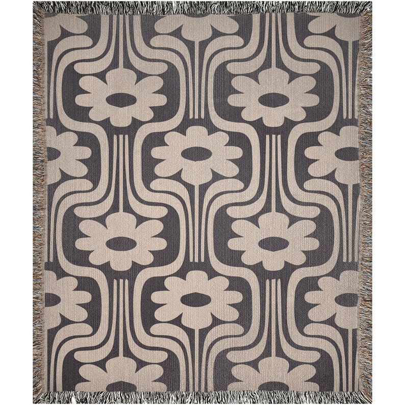 May include: A woven throw blanket with a geometric pattern of stylized flowers in beige on a dark gray background.
