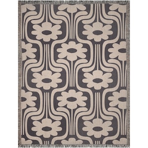 May include: A woven throw blanket with a geometric pattern of stylized flowers in beige on a charcoal background. The blanket has fringe on all sides.
