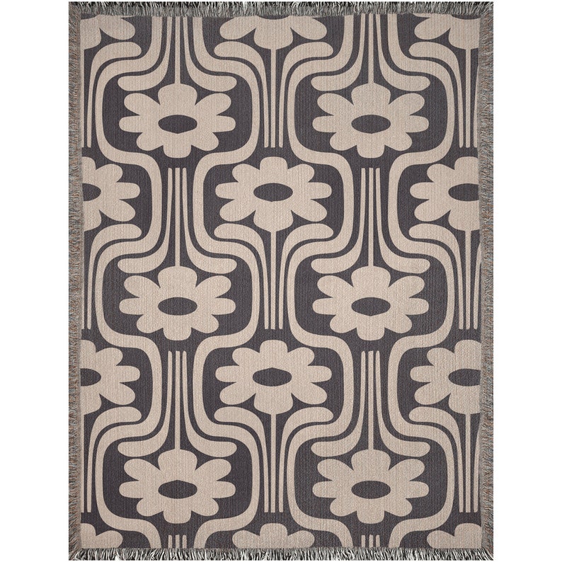 May include: A woven throw blanket with a geometric pattern of stylized flowers in beige on a charcoal background. The blanket has fringe on all sides.