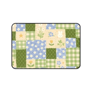 Könnte beinhalten: Rechteckiges Mousepad mit Patchwork-Design. Das Design zeigt Quadrate mit hellblauen Blumenmustern, grünem Vichy-Karo und cremefarbenen Quadraten mit Blumen- und Hasenillustrationen. Die Ränder sind schwarz.