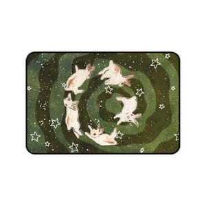 May include: Rectangular mousepad featuring a whimsical illustration of five rabbits in a circle, set against a swirling green and white background with scattered white stars. The rabbits are depicted in a playful, cartoonish style.