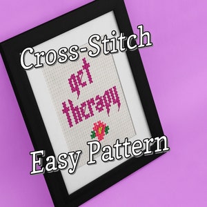 Könnte beinhalten: Ein gerahmtes Kreuzstichmuster mit dem Text "get therapy" in rosa Schrift und einer kleinen rosa Blume. Der Rahmen ist schwarz und der Hintergrund ist rosa.