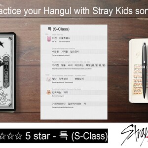 May include: A notebook with a black and white dragon design, a notepad with Hangul lyrics, and a pen on a wooden surface. The text "Practice your Hangul with Stray Kids songs" is at the top. The image also includes the Stray Kids logo.