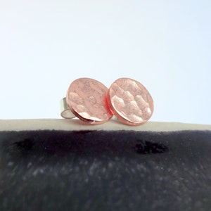 May include: A pair of rose gold hammered circle stud earrings. The earrings are made of metal and have a textured surface.