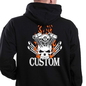 Può includere: Felpa con cappuccio nera con un grafico di teschio e motore bianco con fiamme arancioni e la parola "CUSTOM" stampata sul retro.
