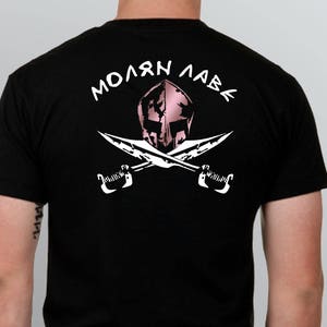 Peut inclure: T-shirt noir avec un graphique blanc d'un casque spartiate avec des épées croisées et le texte "ΜΟΛΩΝ ΛΑΒΕ" en blanc.