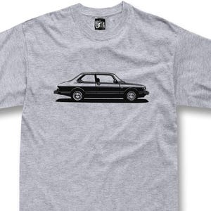 May include: A gray t-shirt featuring a black illustration of a classic car. The car is a two-door coupe with detailed wheels and side paneling. The shirt has a crew neck and a small logo on the upper chest.