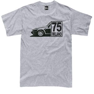 Könnte beinhalten: Hellgraues T-Shirt mit einer schwarzen Grafik eines Autos und dem Text "75 MILANO" in einem schwarzen Rechteck. Die Autografik befindet sich auf der linken Seite des T-Shirts.