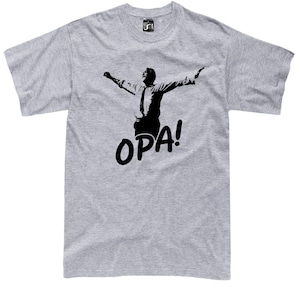Può includere: T-shirt grigio chiaro con una silhouette nera di una persona con le braccia tese e la parola "OPA!" in lettere nere in grassetto. La maglietta ha un girocollo e maniche corte.
