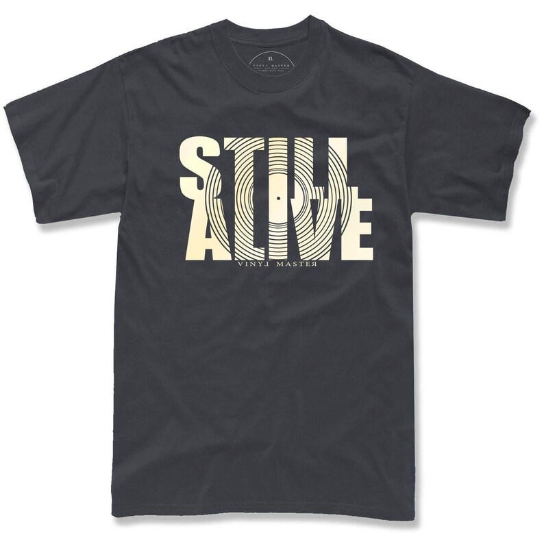 A black t-shirt with a graphic design featuring the text "STILL ALIVE" in a stylized font, with the word "VINYL" underneath.