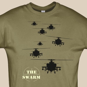 Op de afbeelding: Olijfgroene sweatshirt met een zwarte afbeelding van verschillende helikopters in vlucht. De tekst "THE SWARM" is in een cirkelvormig ontwerp aan de onderkant gedrukt. Het ontwerp is gecentreerd op de voorkant.