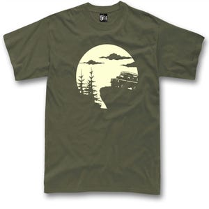 May include: Khaki green t-shirt with a cream-coloured graphic depicting a 4x4 vehicle on a cliff edge under a full moon. The design includes trees and clouds, creating an outdoor adventure theme. The shirt has short sleeves and a crew neck.