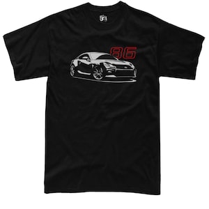 Peut inclure: T-shirt noir avec un dessin blanc d'une voiture de sport et le numéro "86" en rouge. La voiture est représentée avec des roues et des lignes de carrosserie détaillées. Le t-shirt a un col rond et des manches courtes.