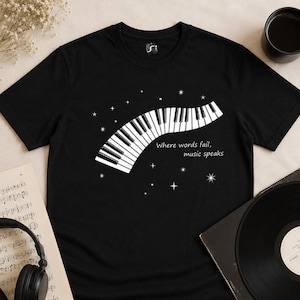 Pode incluir: Camiseta preta com um design de teclado de piano branco e o texto "Where words fail, music speaks". O design inclui estrelas. Um disco de vinil, partituras e fones de ouvido tamb&eacute;m s&atilde;o vis&iacute;veis.