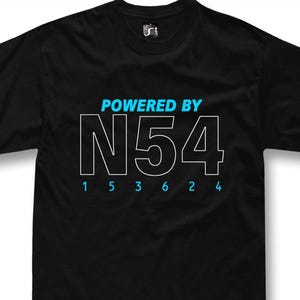 Può includere: T-shirt nero con la scritta "POWERED BY N54" in bianco e blu. Sotto il grande "N54" bianco ci sono i numeri blu "1 5 3 6 2 4". La maglietta ha uno scollo tondo e un piccolo logo in alto a destra.