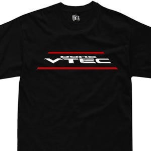Może przedstawiać: Czarny t-shirt z białym i czerwonym wzorem graficznym. Wzór zawiera napis "VTEC" w kolorze białym, z napisem "DOHC" powyżej i czerwoną linią poniżej. Koszulka ma klasyczny okrągły dekolt i krótkie rękawy.