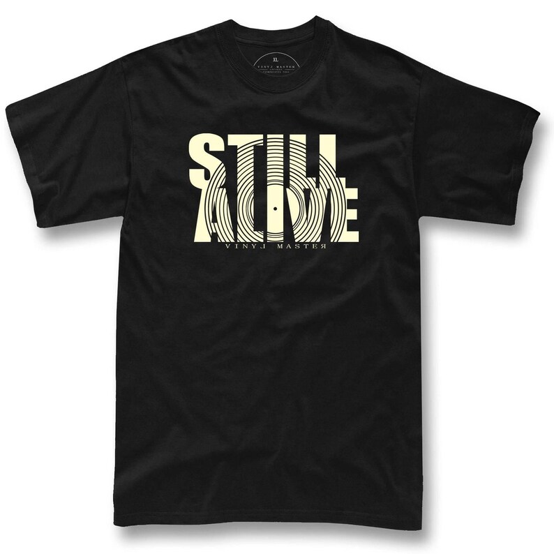 A black t-shirt with a graphic design featuring the text "STILL ALIVE" and "vinyl master" printed on it.