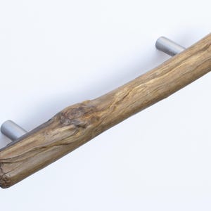 May include: A rustic wooden cabinet pull with a natural wood finish and silver metal accents. The pull is shaped like a branch with a knot in the center.