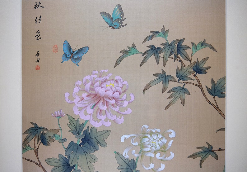 Puede incluir: Pintura de inspiraci&oacute;n asi&aacute;tica con dos mariposas azules, crisantemos rosas y blancos, y follaje verde sobre un fondo beige. La obra de arte incluye caligraf&iacute;a y un sello rojo.