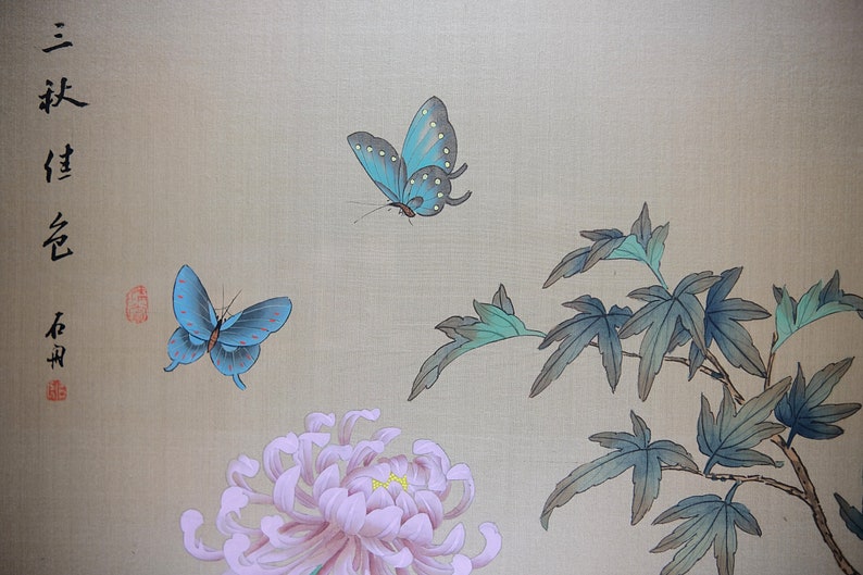 Puede incluir: Una pintura de inspiraci&oacute;n asi&aacute;tica con dos mariposas azules con puntos blancos, un gran crisantemo rosa y hojas verdes y azules. El fondo es de color beige claro y hay caligraf&iacute;a asi&aacute;tica en el lado izquierdo.