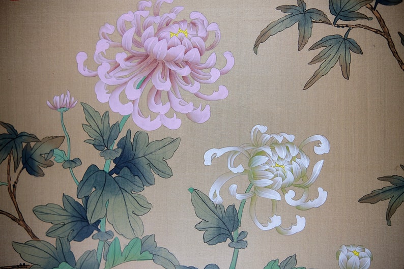 Puede incluir: Obra de arte floral con grandes crisantemos estilizados en tonos rosa y blanco, con centros amarillos. Las flores se encuentran sobre un fondo beige, con hojas y tallos verdes. La obra tiene una est&eacute;tica tradicional de inspiraci&oacute;n asi&aacute;tica.