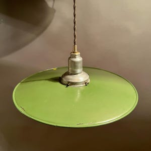 May include: A vintage-style pendant light with a round, bright green shade. The shade is attached to a silver-colored fixture and a twisted brown cord. The light fixture is suspended from the ceiling, showcasing a retro aesthetic.