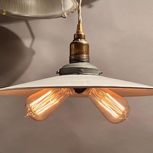 May include: A white porcelain pendant light fixture with two exposed filament light bulbs. The fixture has a simple, industrial design and is suspended from a single cord.