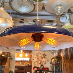 May include: A blue and white enamel pendant light fixture with three exposed filament light bulbs. The light fixture is hanging from a ceiling and is surrounded by other light fixtures.
