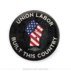 May include: A black and white button with a raised fist holding an American flag. The text "Union Labor Built This Country" is written around the fist in a white circle.