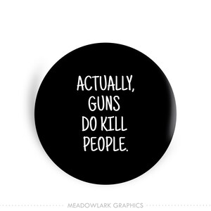 May include: A black round button with the white text "ACTUALLY, GUNS DO KILL PEOPLE." The button has a white border and a shadow effect. The words are in a sans-serif font.