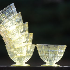 May include: A stack of six clear yellow glass dessert bowls with a fluted design. The bowls are stacked in a pyramid shape, with the largest bowl at the bottom and the smallest bowl at the top. A single bowl is sitting on the table to the right of the stack.