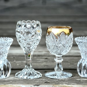 Può includere: Quattro vasi di vetro trasparente con intricati disegni di vetro tagliato. Due dei vasi sono più alti e hanno uno stelo, mentre gli altri due sono più bassi e hanno una base rotonda.