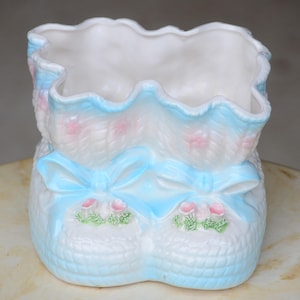 Könnte beinhalten: Ein blauer und weißer Keramik-Pflanztopf in Form eines Babyschuhs mit rosa Blumenmotiven.