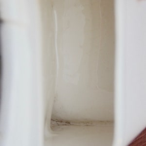 May include: Close-up of the inside of a white ceramic jug. The inside of the jug has a dark grey stain along the bottom edge.