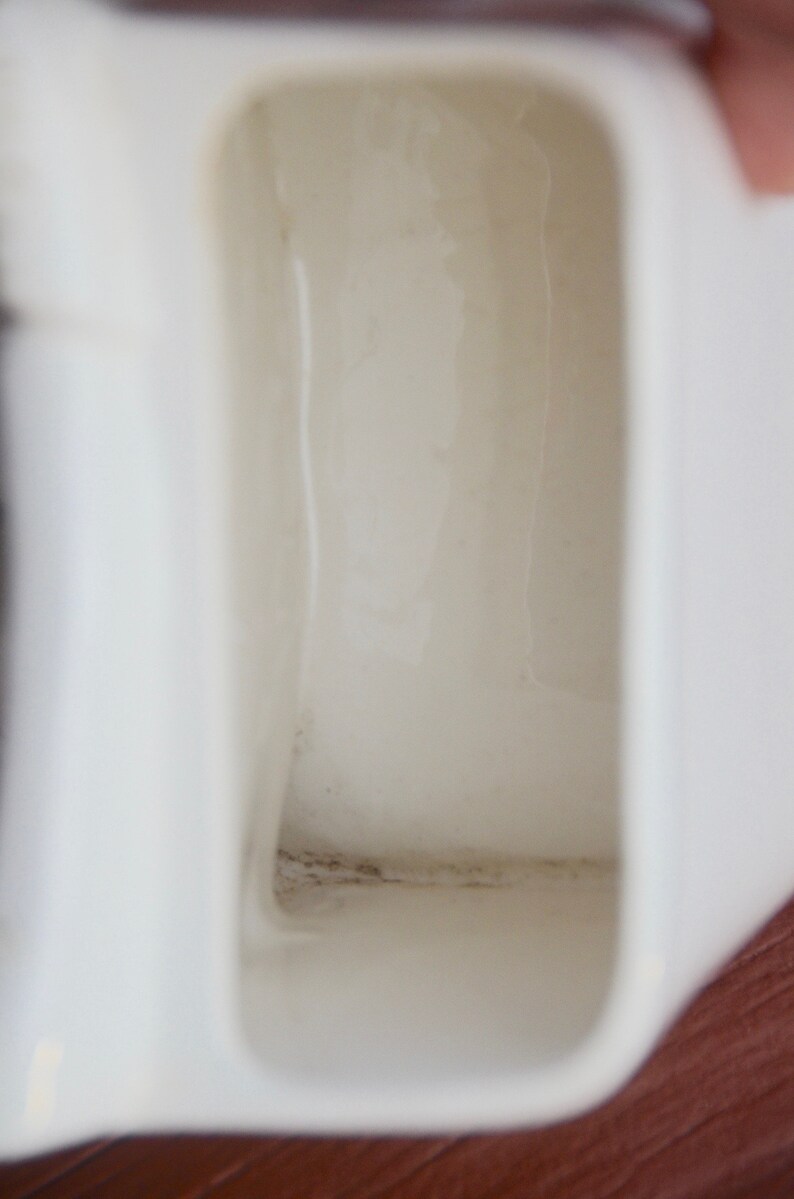 May include: Close-up of the inside of a white ceramic jug. The inside of the jug has a dark grey stain along the bottom edge.