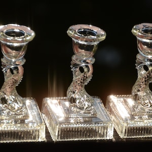 May include: Three clear glass candle holders with a fish design. Each holder has a square base with a raised edge and a fish-shaped stem.