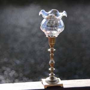 Puede incluir: Un portavelas de vidrio transparente con un borde superior con volantes se asienta sobre un candelabro de latón con una base cuadrada.