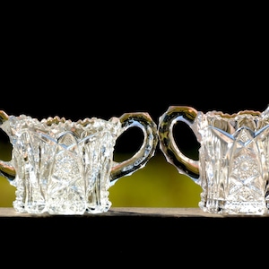 Puede incluir: Un juego de dos jarras de azúcar y crema de vidrio transparente con intrincados diseños de vidrio cortado. Las jarras tienen un aspecto vintage y son perfectas para añadir un toque de elegancia a cualquier mesa.