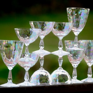 Può includere: Un set di otto calici e flute da champagne in vetro iridescente impilati a forma di piramide. I bicchieri hanno una superficie testurizzata, con bolle e un bagliore simile all'arcobaleno.