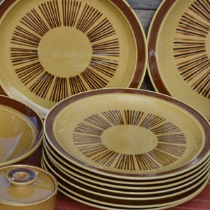 Puede incluir: Un juego de vajilla de cerámica marrón y beige con un patrón geométrico. El juego incluye platos, cuencos y una fuente cubierta.