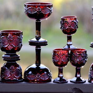 May include: A collection of ten red glass goblets and bowls with intricate patterns. The goblets are arranged in a pyramid shape, with the largest goblet at the top and the smallest goblet at the bottom. The bowls are placed at the base of the pyramid.