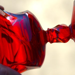 May include: A red glass goblet with a wide base and a flared top. The goblet has a unique, wavy design.