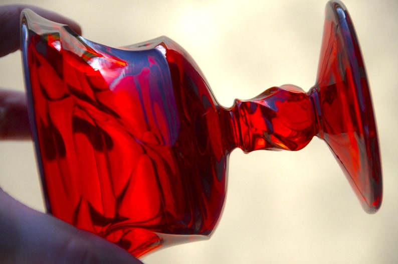 May include: A red glass goblet with a wide base and a flared top. The goblet has a unique, wavy design.