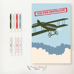 May include: Aviation-themed party game with a blue and cream background. The game features a green biplane illustration with the text "PIN THE PROPELLER" in a red rectangle. Includes several propeller cutouts in various colours.